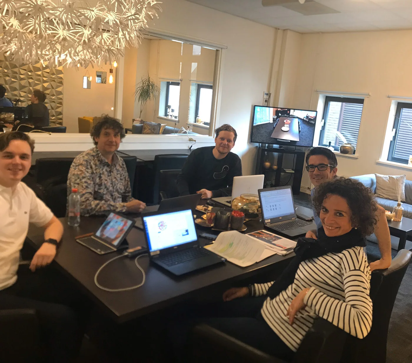 Vijf mensen werken samen aan een tafel met laptops en notities.