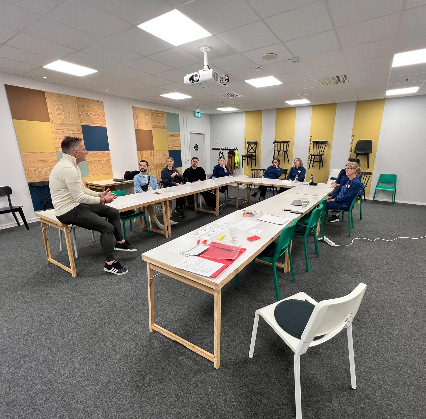 Deelnemers aan een werksessie zitten rond tafels met papier en tekenmateriaal.