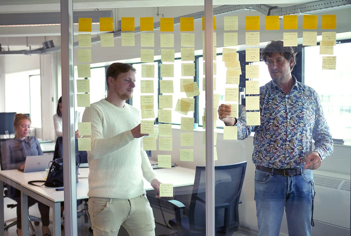 Robert en Frenz ordenen inzichten uit interviews op een glazen wand voor een nieuwe klantreis rond vliegtickets.